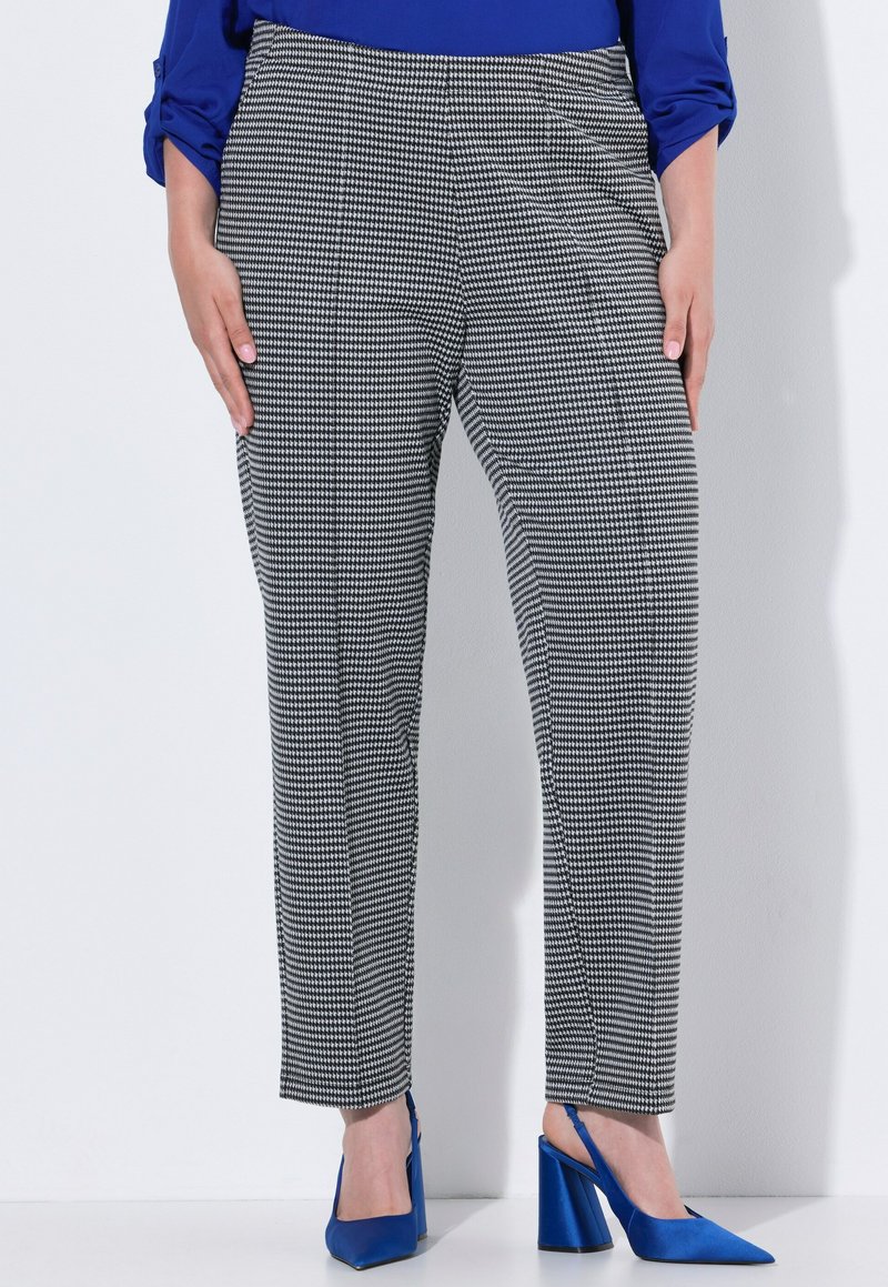 Kalhoty s vzorem houndstooth v černobílém provedení, rovného střihu a jemné textury, doplněné modrými špičatými slingbackmi.