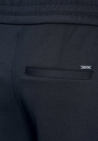 Černé kalhoty z texturované tkaniny s malým stříbrným logem a horizontální zadní kapsou s texturovaným lemem.