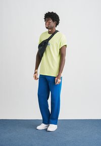 Lime green t-shirt, graphic detail, paired with blue sweatpants. Black crossbody bag accentuates the casual look. White sneakers complete the outfit.