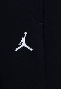 Černá mikina vyrobená z látky, která má výrazné bílé vyšívané logo Jumpman, znázorňující postavu skákající k hodu na koš.