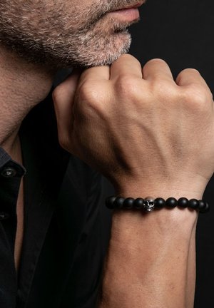 Bracelet en perles noires avec un accent en skull argenté. Fini mat sur les perles, forme ronde et design élastique pour un ajustement réglable.