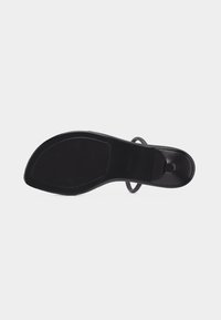 Μαύρη επίπεδη σόλα σανδάλι με υφή για καλύτερο κράτημα, λεπτό λουρί ορατό στο πλάι και στενό τακούνι, πάνω σε απλό φωτεινό φόντο.