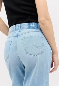 Light blue denim jeans with a high waist and five pockets. Features include a stitched triangle pattern on back pockets and a logo on the waistband.