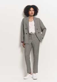 Blazer doppiopetto a quadri grigi, con pantaloni slim-fit abbinati, abbinato a una t-shirt bianca con grafiche e sneakers bianche.