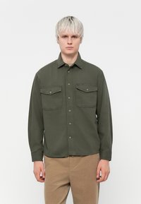 Olive green button-up shirt with two front pockets, long sleeves, a collar, and a relaxed fit. Mildly textured fabric.