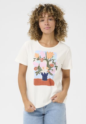 T-shirt en coton crème avec un design floral coloré sur le devant, comprenant un vase bleu et un accent rouge en dessous. Manches courtes, coupe décontractée.