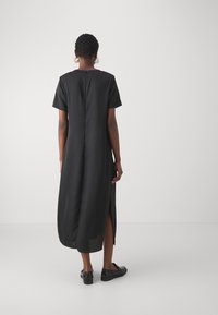 Rochie neagră cu mâneci scurte, tiv lung, slituri laterale și croi drept. Fabricată dintr-un material ușor, având o închidere discretă la spate.
