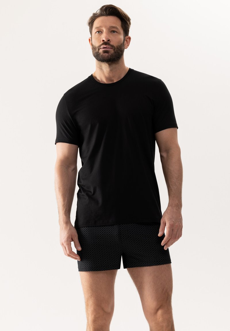 Černé tričko s krátkým rukávem vyrobené z měkké tkaniny; v kombinaci s černými sportovními šortkami s vzorem obsahujícím hexagonální design.