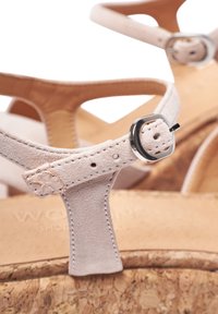 Light beige suede sandals with a cork sole. Thin straps with a silver-tone buckle and stitching details. Textured footbed visible behind straps.