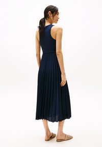 Rochie maxi plisată de culoare albastru închis, cu un corset ajustat și talie elastică, realizată dintr-un material neted. Purtați-o cu pantofi slip-on de culoare deschisă.