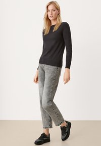 Schwarzer Pullover mit langen Ärmeln und geripptem Saum, kombiniert mit hellgrauen, schmal geschnittenen Jeans. Schwarze Sneaker mit strukturierten Details runden das Outfit ab.