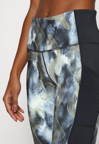 Vysoké legíny černé barvy s abstraktním vzorem v modré a zlaté barvě. Obsahují hladkou strukturu a jemné švy, které zlepšují přizpůsobení a pohyb.