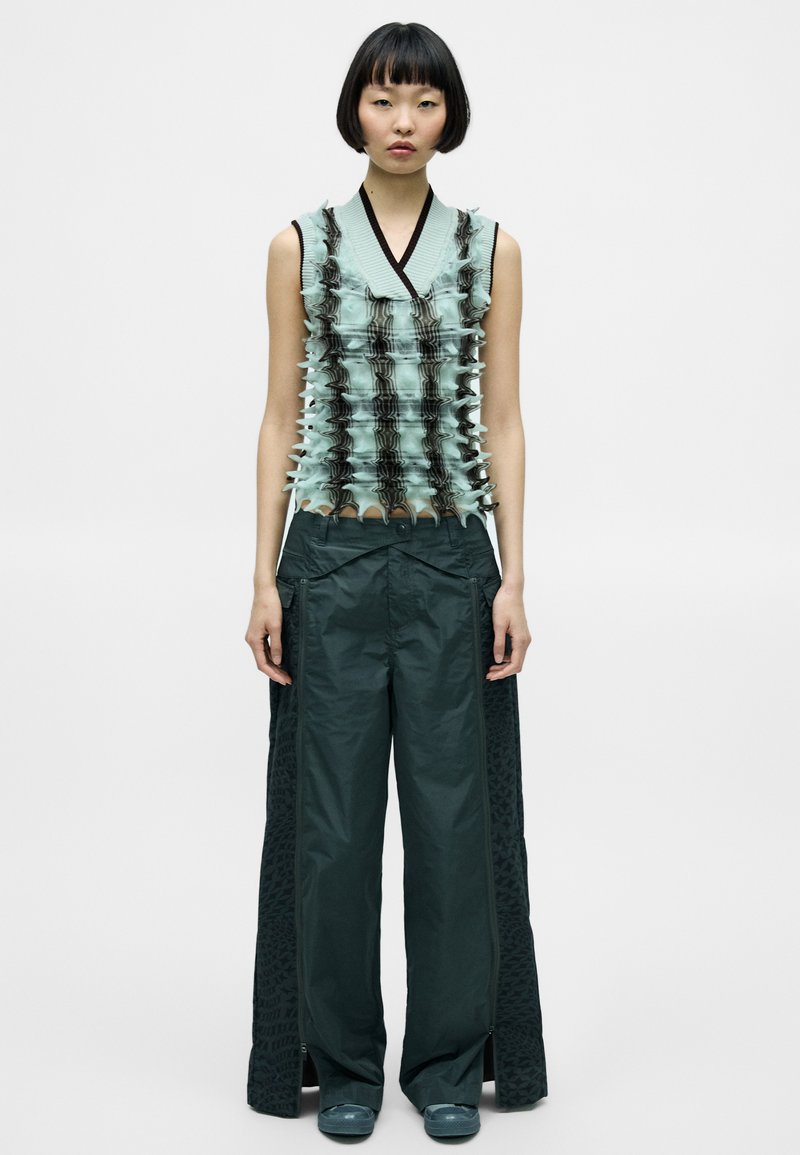 Ljust blå strukturerad ärmlös topp med mörka volangdetaljer, paired med mörkgröna vida byxor med sidoredskap och mönstrade sidopaneler.