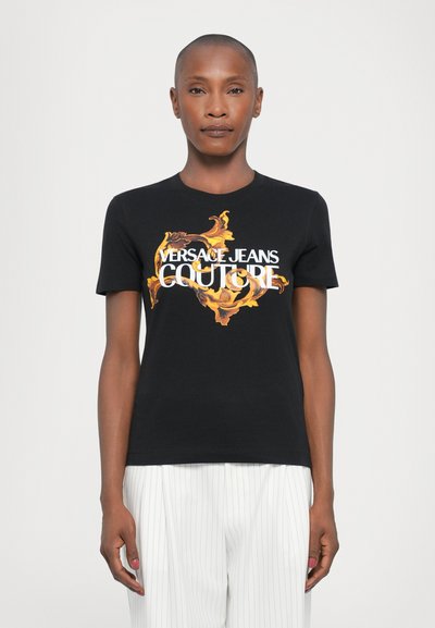 T-shirt en coton noir avec un design baroque coloré et le texte "VERSACE JEANS COUTURE" en blanc. Manches courtes, col rond.