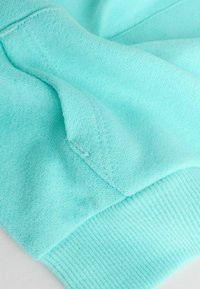 Mintunvihreä collegepaita kangas, joka on pehmeä ja siinä on resorit hihansuissa sekä näkyvä sauman yksityiskohta.