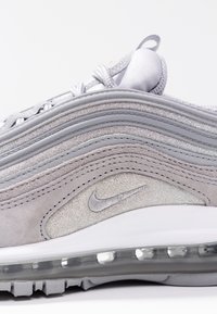 Nike Air Max 97-sneaker i ljusgrå, med lager av mocka och metalliska accenter, nedsänkt logotyp och synlig luftkudde i sulan.