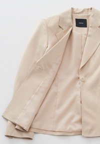 Blazer beige realizzato in tessuto liscio. Presenta un colletto a scollo a V, chiusura con un singolo bottone e una fodera interna in raso.