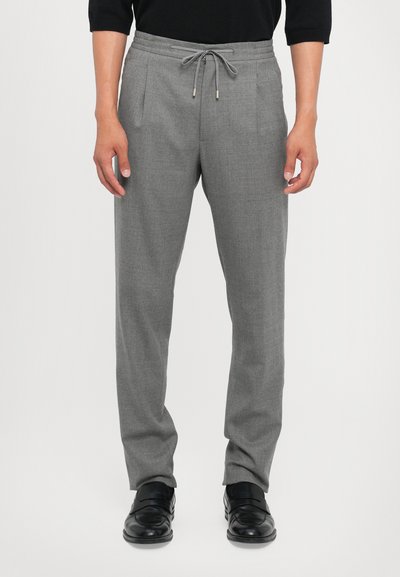 Pantalons gris sur mesure avec taille à cordon, deux plis à l'avant et texture lisse, associés à des mocassins noirs.