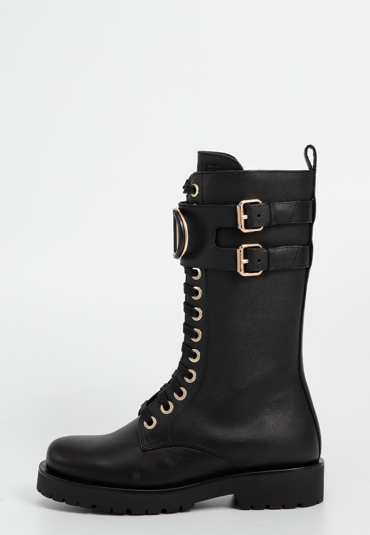 Botte de combat en cuir noir avec matériel doré, lacets à l'avant, accents de double boucle sur la tige, et semelle robuste pour une traction optimale.