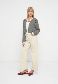 Giacca cropped a righe bianche e nere, top bianco, pantaloni beige a gamba larga e scarpe basse rosse. Concentrati sulle trame e sui colori a contrasto.