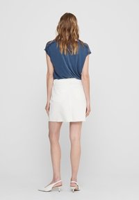 Haut bleu à manches courtes avec des accents en dentelle, associé à une mini-jupe en denim blanche, dotée de deux poches arrière et d'un ourlet effiloché. Chaussures blanches à talons.