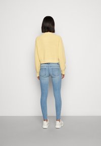 Beskurad gul stickad tröja med ribbad nederkant, i kombination med ljusblå skinny jeans och vita sneakers, sedd bakifrån.