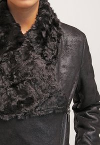 Chaqueta de cuero negra con un suave y acogedor cuello de piel sintética. El diseño incluye un bolsillo con cremallera en el lateral y un acabado liso y texturizado.