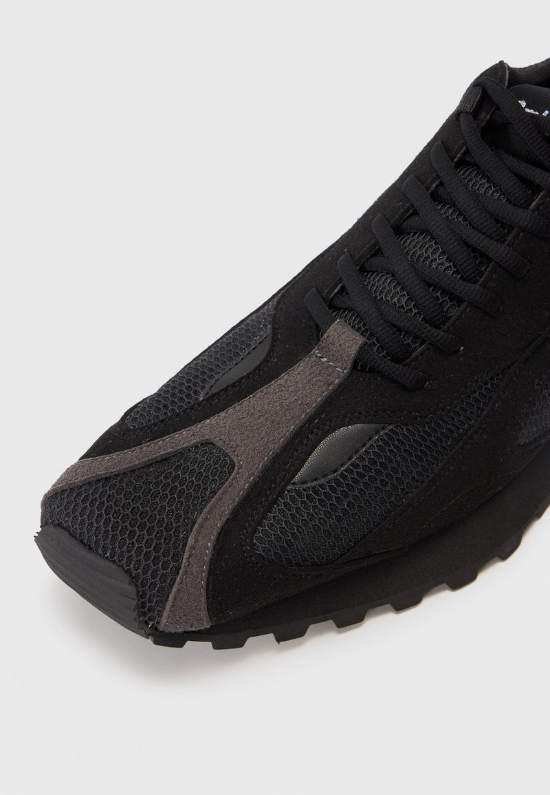 Svart atletisk sko med mesh- och mockakvalitet, snörningsdesign och en distinkt grå accent på ovansidan och sulan.