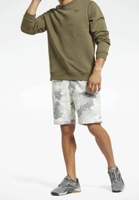 Olivově zelená mikina s žebrovanými manžetami a lemem, spárovaná se světle šedými šortkami s texturovaným abstraktním vzorem. Šedé sportovní boty.