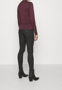 Haut long à manches maroon avec un col rond, associé à un pantalon slim noir et des bottines noires à finition texturée et talons bloc.