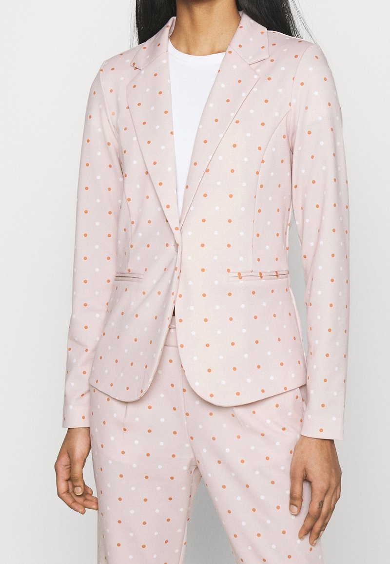 Ljusrosa kavaj med vita och orange prickar, enknappsslutning, slitsiga kragar och två framfickor. Slät tygstruktur.