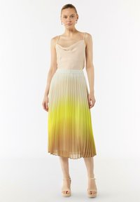 Plisowana spódnica midi w gradientowych odcieniach beżu do żółtego, zestawiona z jasną beżową bluzką z dekoltem typu cowl. Gładki materiał o miękkiej fakturze.