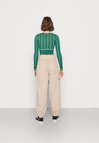 Groen gestreept crop top met lange mouwen gecombineerd met beige cargobroek; zwarte platformsneakers zichtbaar; gladde textuur, casual ontwerp.