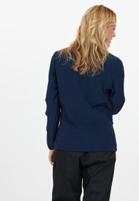 Mörkblå softshell-jacka med en slät textur, figurnära design och diskreta sömmar, i kombination med svarta vattentäta byxor.