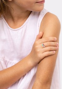 L'anello d'argento presenta piccoli accenti di pietre preziose rosse e verdi, indossato su una mano con pelle chiara. Lo sfondo è neutro per mettere in risalto i gioielli.