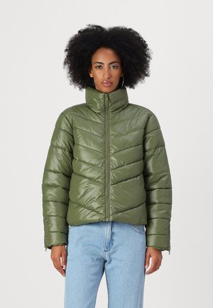 Groene pufferjack met hoge kraag, zigzagpatroon en ritssluiting. Gladde, glanzende stof met elastische manchetten, gedragen over lichte denim.
