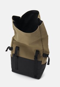 Sac à dos grand, vert olive et noir, avec rabat supérieur ouvert, sangles noires réglables et boucles latérales, sur fond uni.