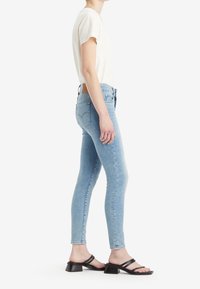 Ljusblå skinny jeans med subtila blekningar, kombinerade med en krämfärgad kortärmad topp och svarta klacksandaler. Jeansen har en klassisk fem-fickdesign.