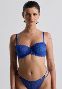 Set di lingerie in pizzo blu composto da un reggiseno imbottito con motivi floreali, bordi ondulati e spalline regolabili, abbinato a un perizoma coordinato.