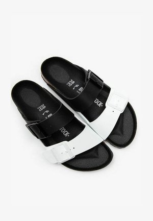 Black and white sandals with adjustable straps and a textured footbed, featuring a smooth upper and durable sole.