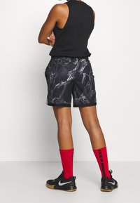 Black sleeveless top, black shorts with marble pattern, red socks with black stripes, and black sneakers with silver logo.