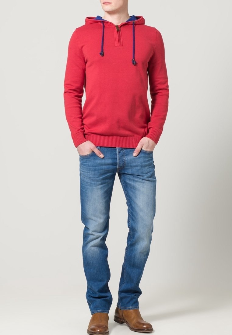 Röd huvtröja med ett blått innertyg, dragkedjeförslutning och snoddar, i kombination med ljusblå jeans och bruna stövlar. Enkel, avslappnad design.