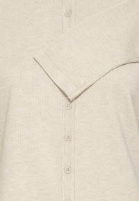Svetlo bež kardigan, rebrasta tekstura, spredaj z gumbi s šestimi gumbi, širok ovratnik in dolgi rokavi.