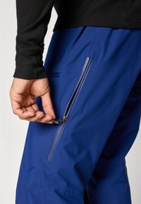 Mėlynos lauko kelnės su užtrauktuku šoniniame kišenyje; lygi tekstūra; matomos siūlės; derinamos su juodu ilgomis rankovėmis palaidine.