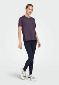 Donkerpaars sportt-shirt met korte mouwen, gecombineerd met marineblauwe leggings en witte sneakers met zwarte accenten en een geribbelde zool.
