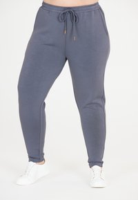 Grå joggarbyxor med dragsko i midjan, sidofickor och avsmalnande ben, tillverkade av mjukt material. Matchas med vita sneakers.