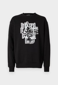 Svart sweatshirt med rund hals och ribbade ärmendingar, med framträdande vit 3D-textgrafik av "KARL LAGERFELD" över framsidan.