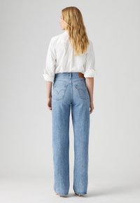 Jean taille haute bleu clair avec une coupe décontractée, ourlets bruts et poches arrière classiques Levi's. Porté avec une chemise blanche à boutons.