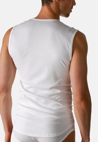 Top bianco senza maniche in morbido cotone. Presenta un design semplice con scollatura tonda e orlo leggermente curvo sul retro.