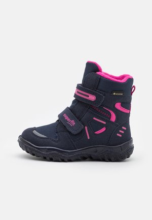 Botte d'hiver pour enfants noire et rose avec des sangles Velcro, étiquette Gore-Tex, semelle texturée et doublure en polaire rose.